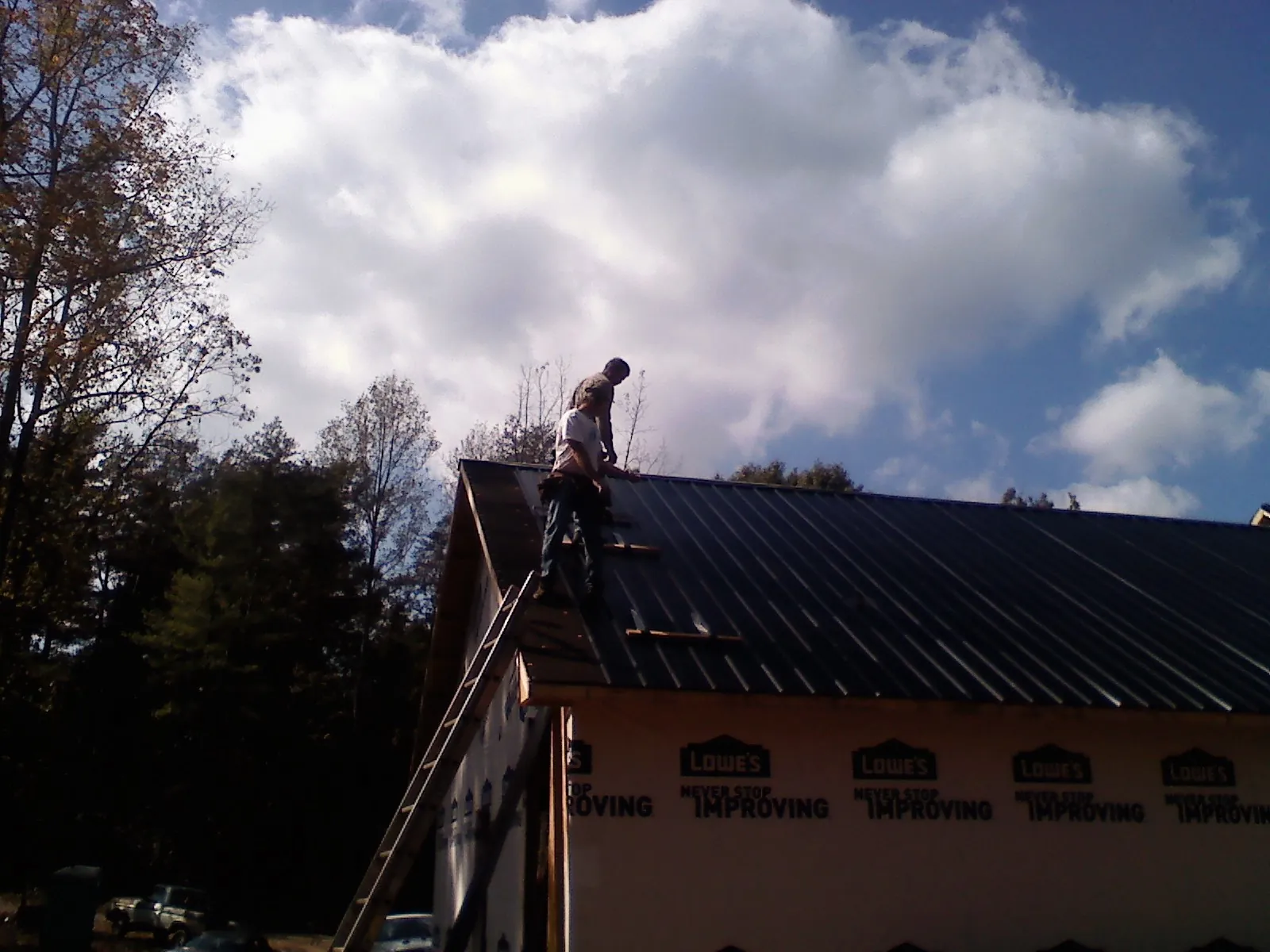 Roofer fastening dark metal panels high against a cloudy sky, from a Roof Inspection job in Forsyth