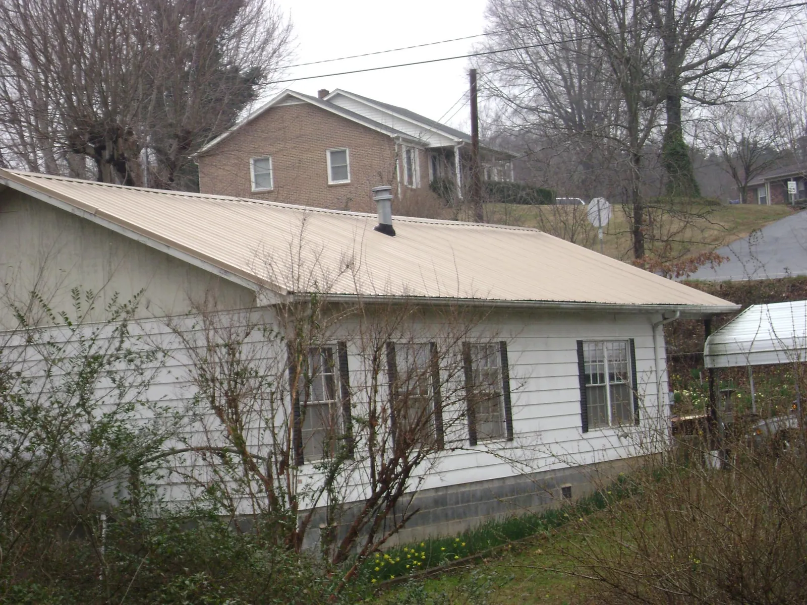 Tan metal roof on a white sided house set into a hillside — Commercial Roofing by Roofing Brothers in Forsyth